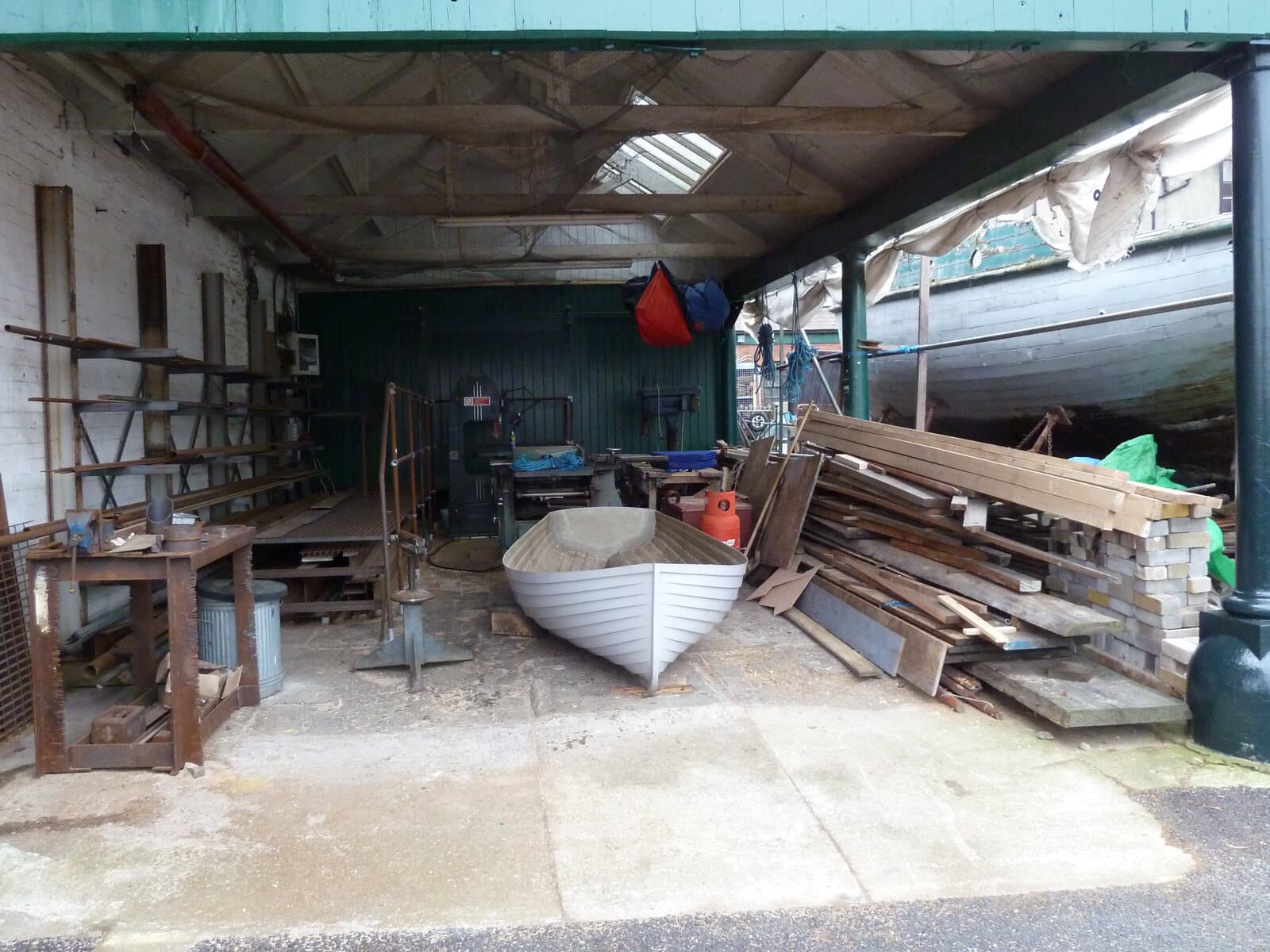 Wooden boats, hulls, and lumber inside an open boatbuilding workshop - representative of the hands-on restoration work at Farley Boat Works.
